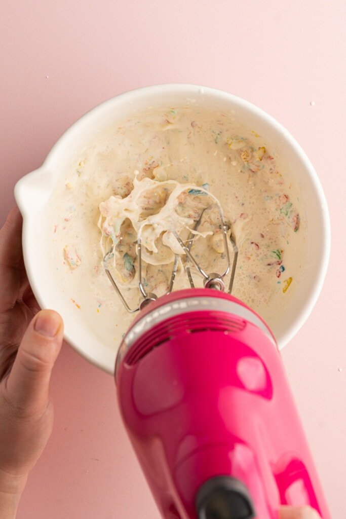 Using a hand mixer to whip together heavy cream, Fruity Pebbles, and powdered sugar