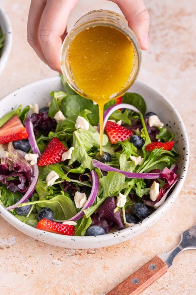 Pouring Maple Dijon Vinaigrette over colorful salad