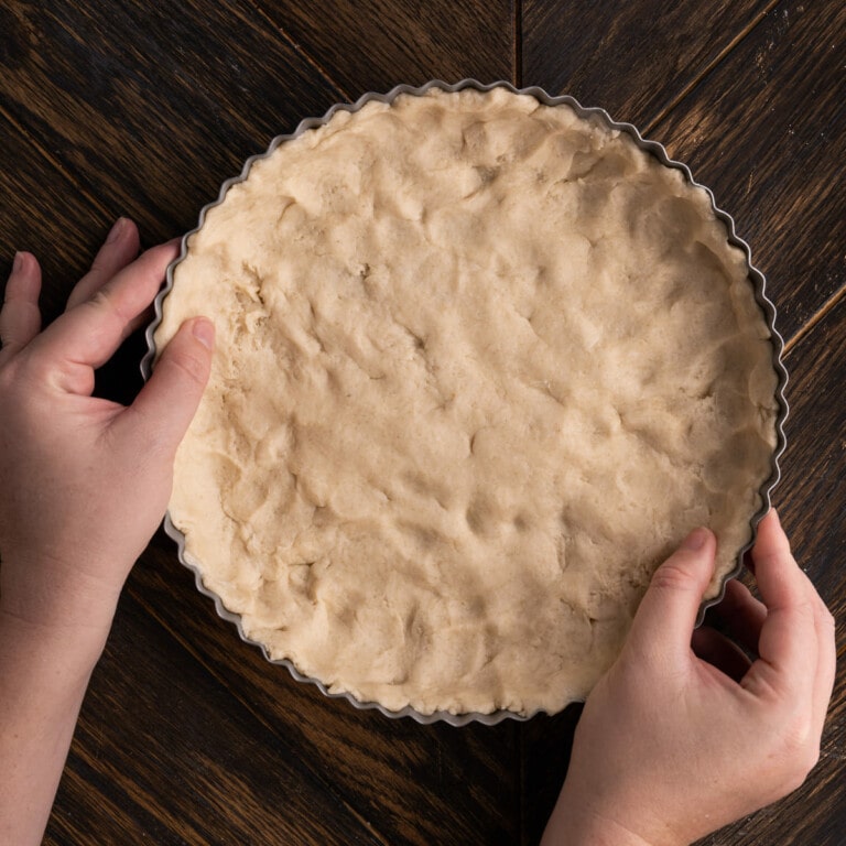 Pushing quiche crust dough into dish to bake