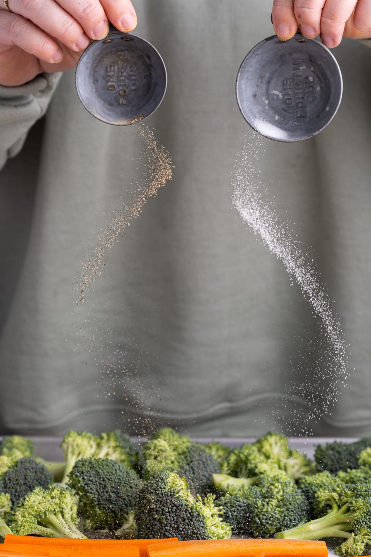 Adding salt and pepper to prepped broccoli and carrots on a baking sheet