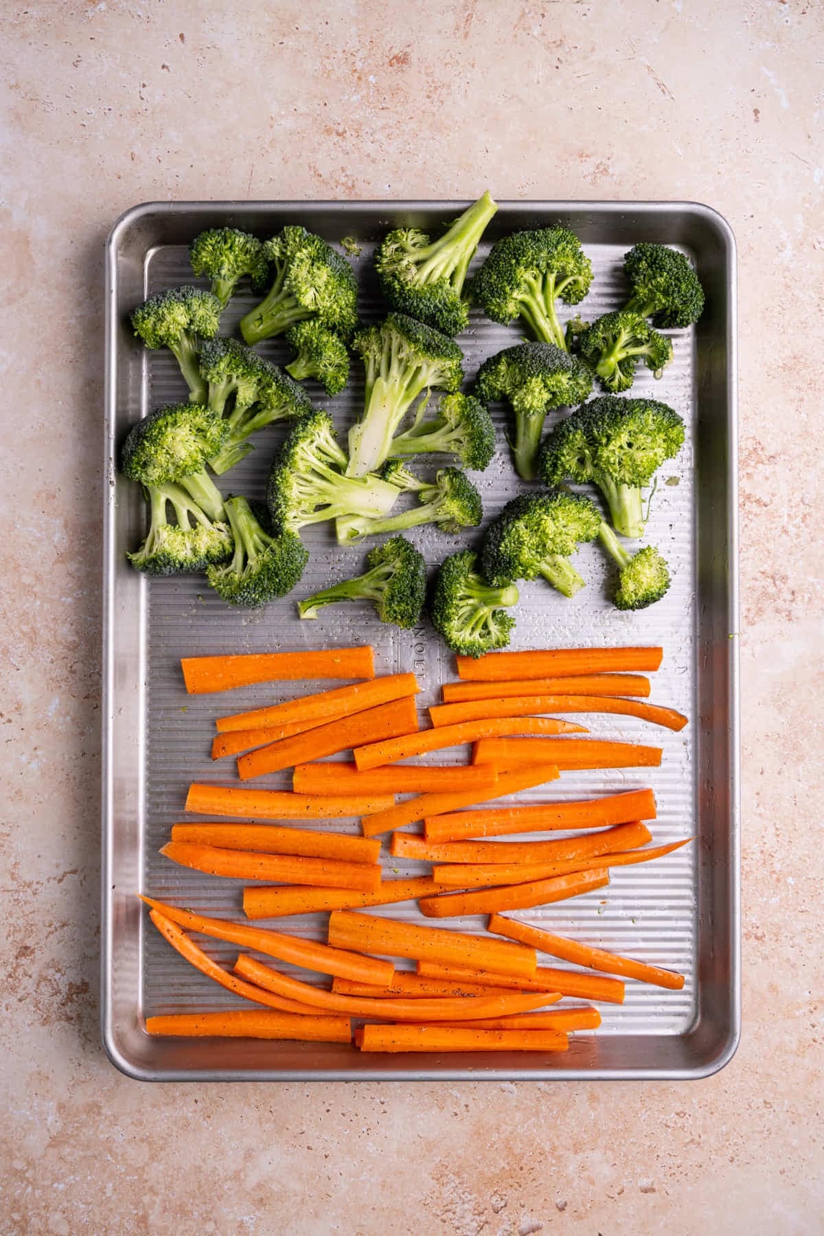 Baking sheet with prepped broccoli and carrots coated in olive oil, salt, and pepper