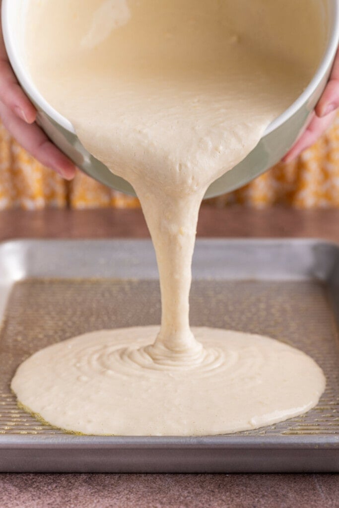 Pouring pancake batter onto a sheet pan to bake in the oven.