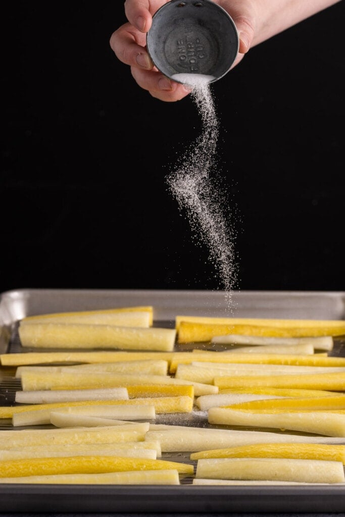 Adding salt to white carrots to roast.