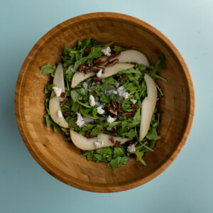 Adding all ingredients for Arugula Pear Salad to a large bowl to toss together