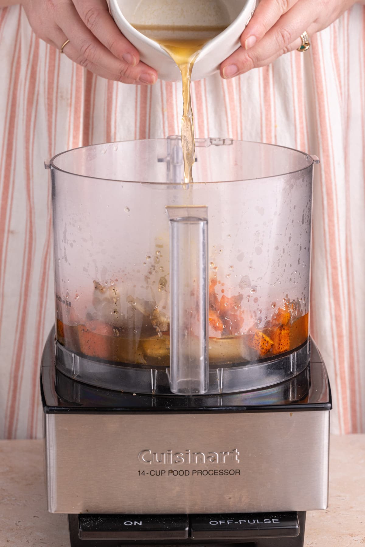 Adding vegetable broth to food processor with roasted carrots to make pasta sauce