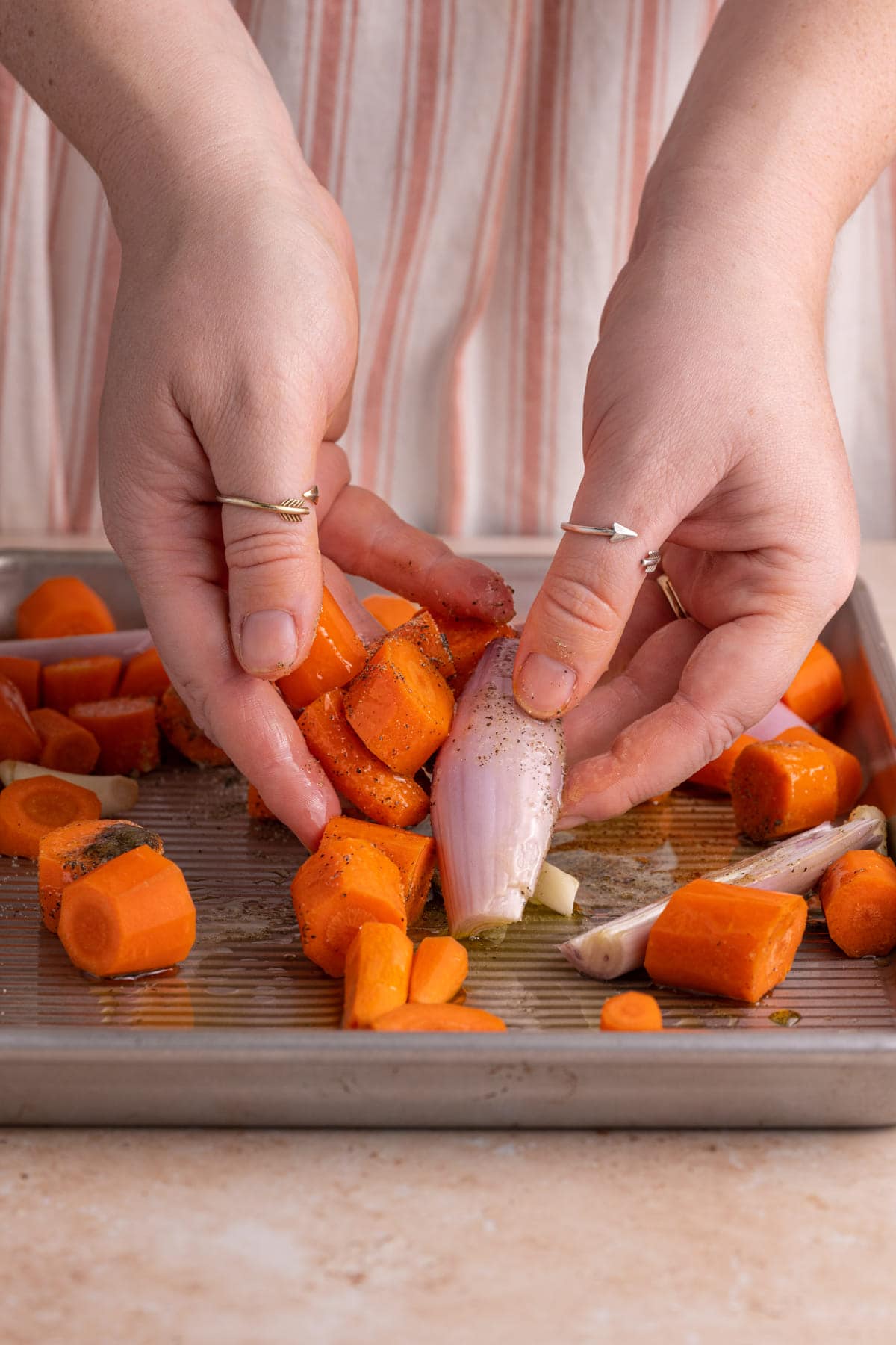 Using clean hands to toss carrots, shallots, and garlic in olive oil, salt, and pepper