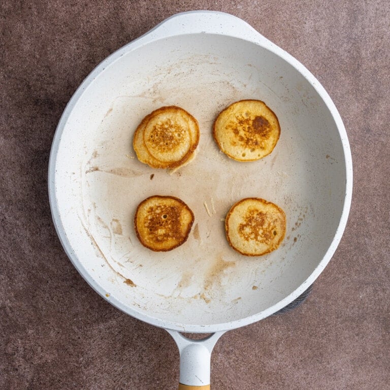 Four mini pancakes frying in a pan