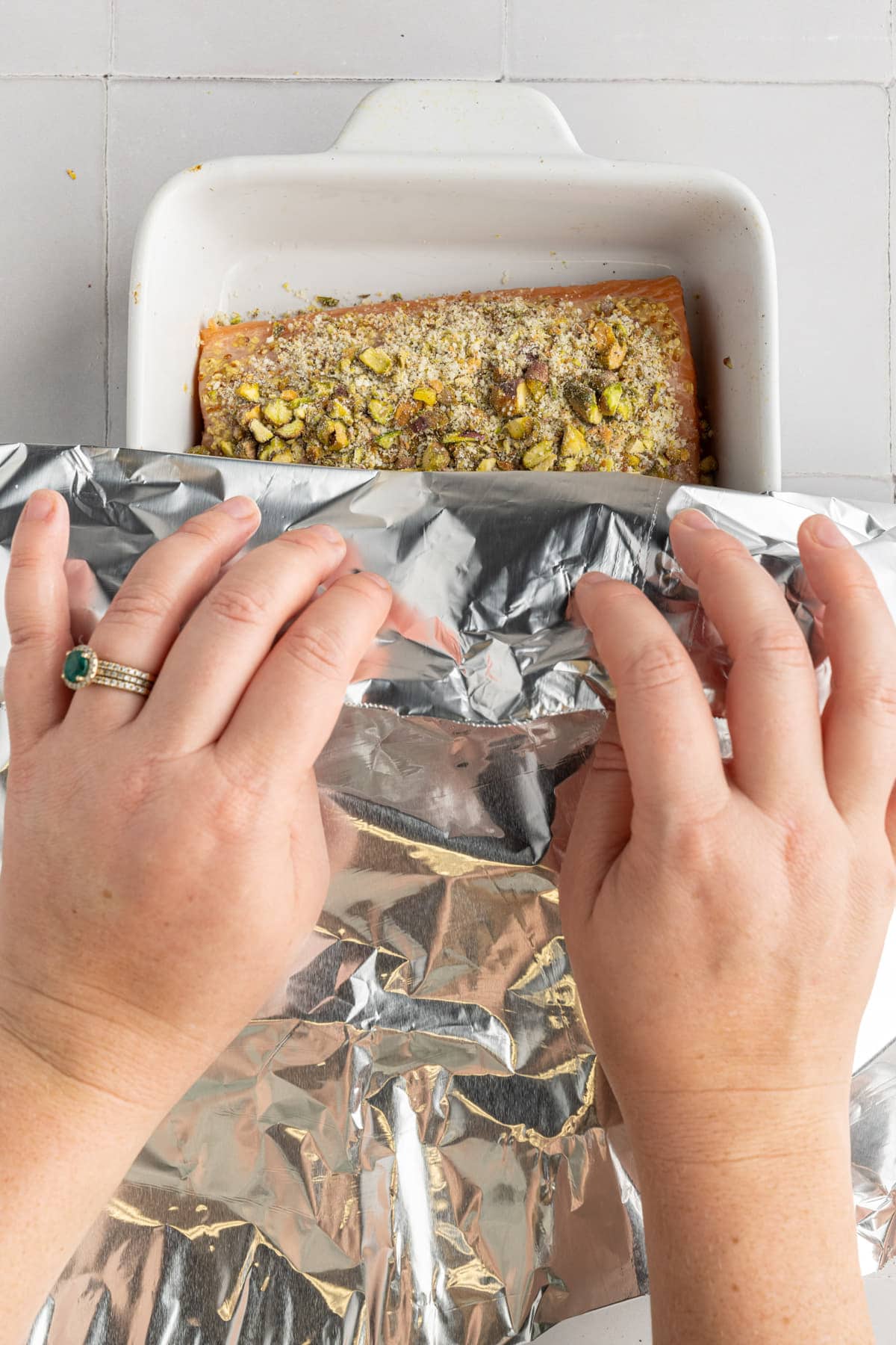 Covering salmon crusted with pistachios with aluminum foil to bake