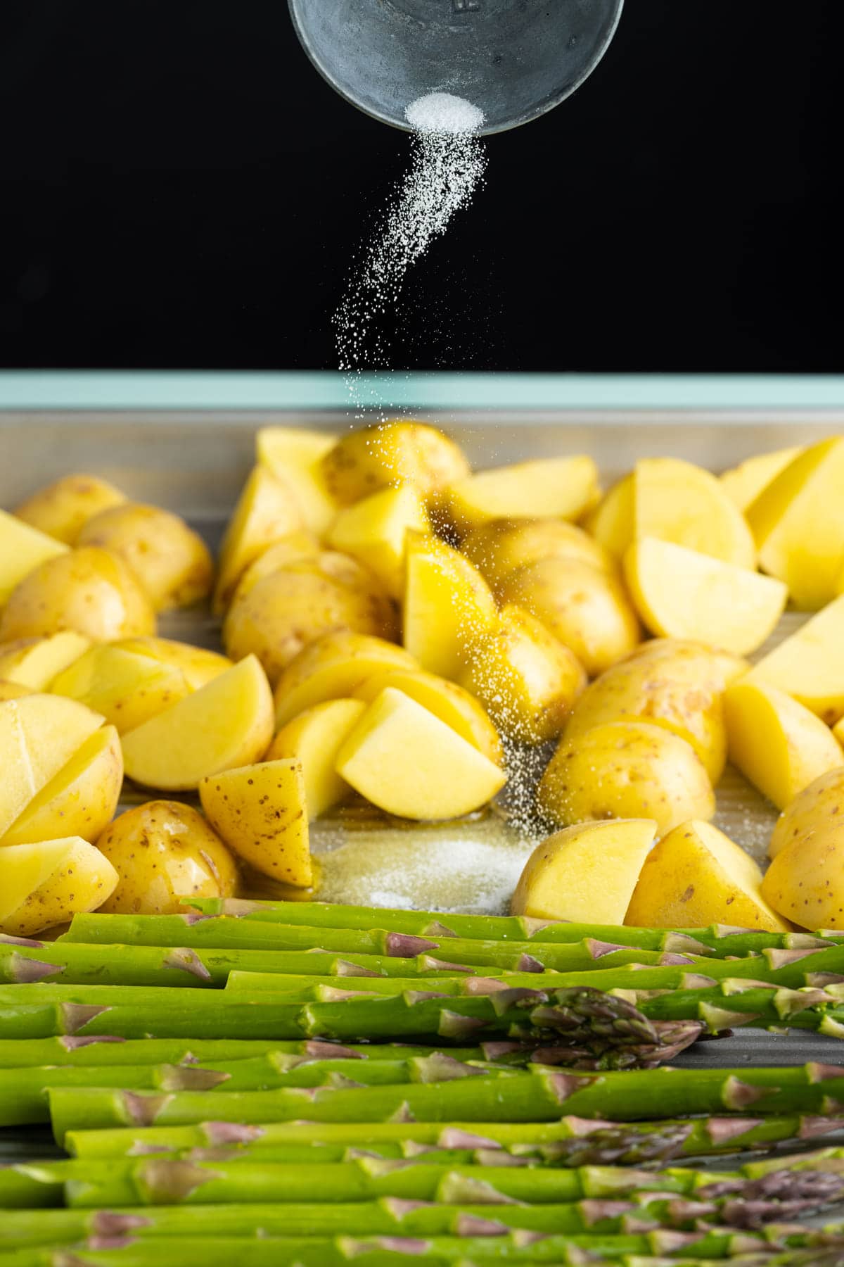 Adding salt to asparagus and potatoes on a sheet pan