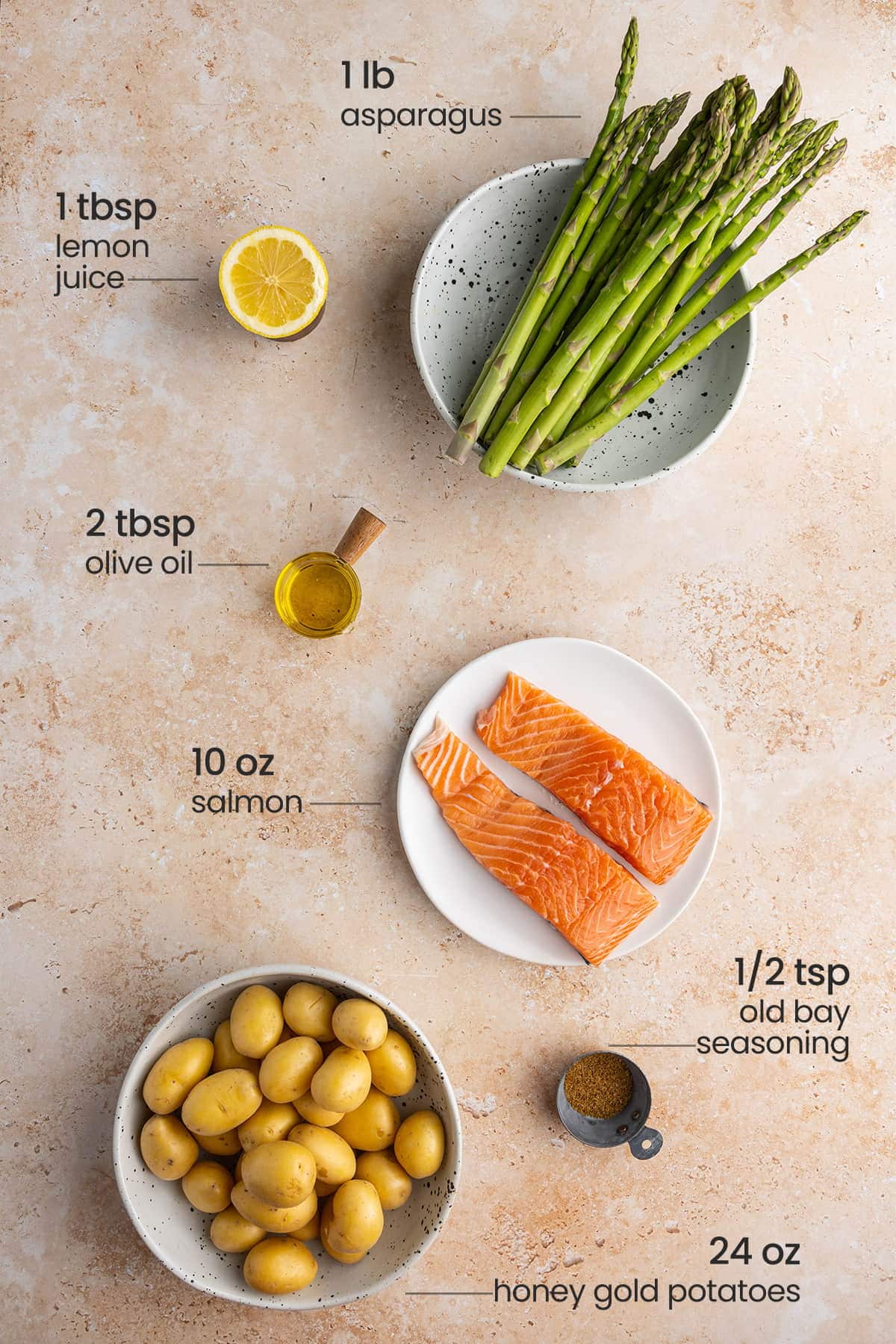 all ingredients for sheet pan salmon, asparagus and potatoes - lemon juice, asparagus, olive oil, salmon, old bay seasoning, honey gold potatoes