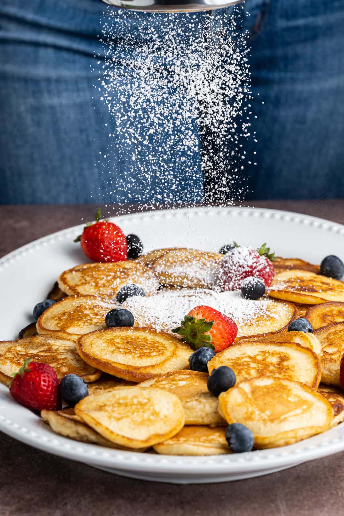 Adding powdered sugar to a platter of silver dollar pancakes