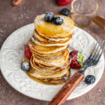 Stack of Silver Dollar Pancakes with powdered sugar, fresh fruit, and maple syrup