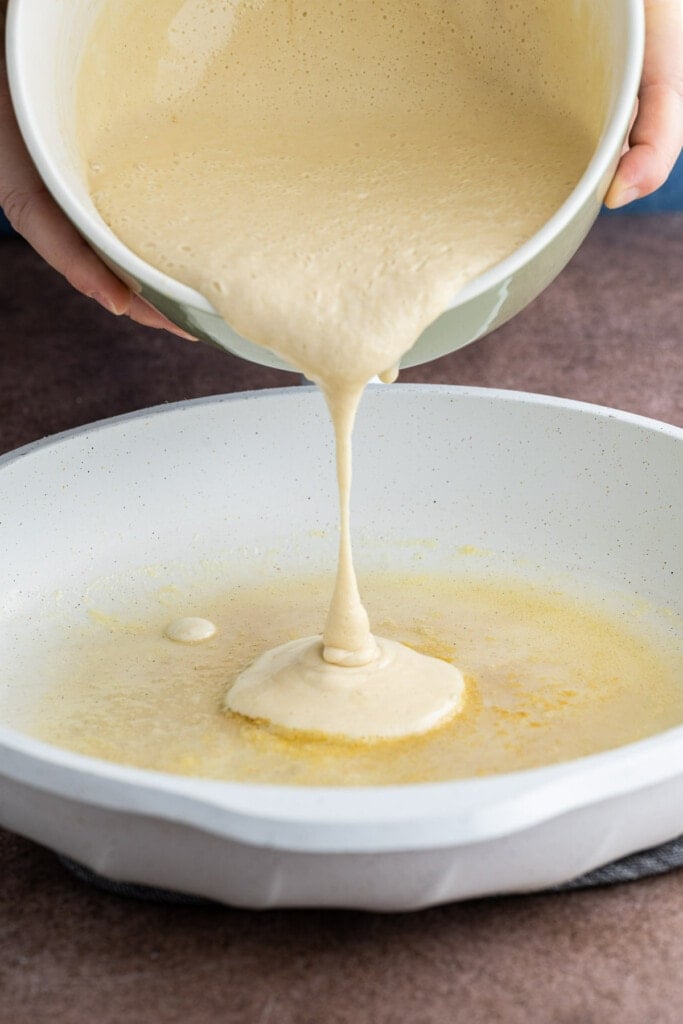Pouring pancake batter into pan to form 2-3 inch pancakes.