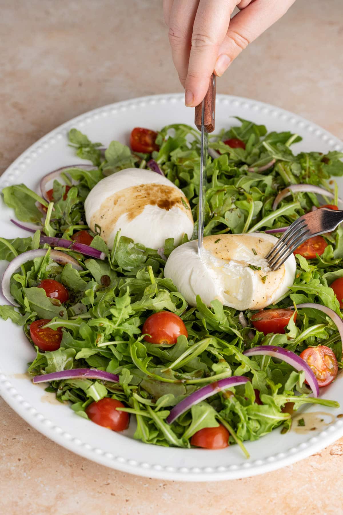 Slicing into Burrata cheese atop arugula-based salad