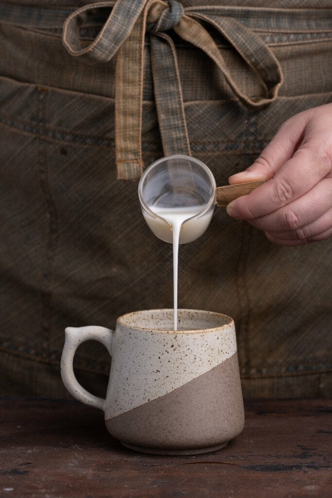 Adding milk to make banana batter in a mug.