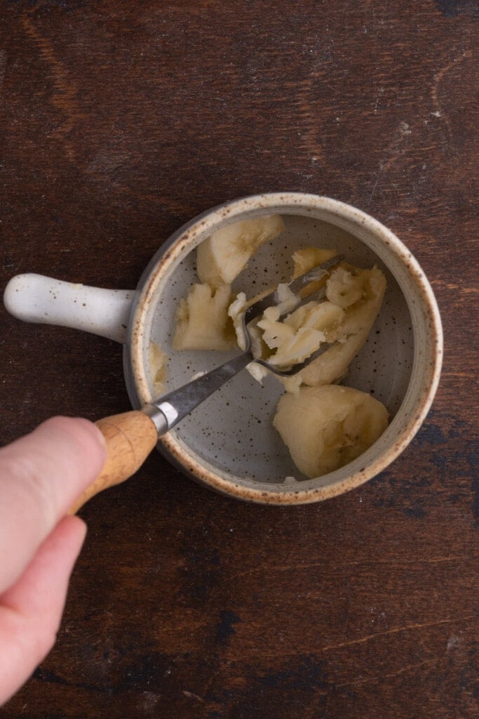 Using fork to smash a banana in a mug.