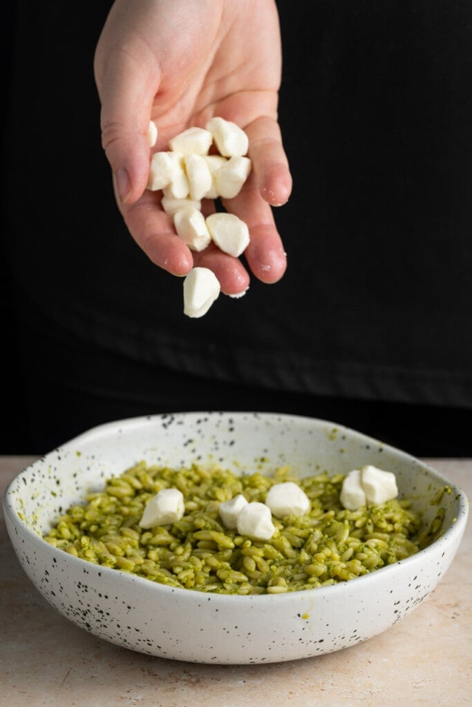 Adding pearled mozzarella to orzo with pesto.
