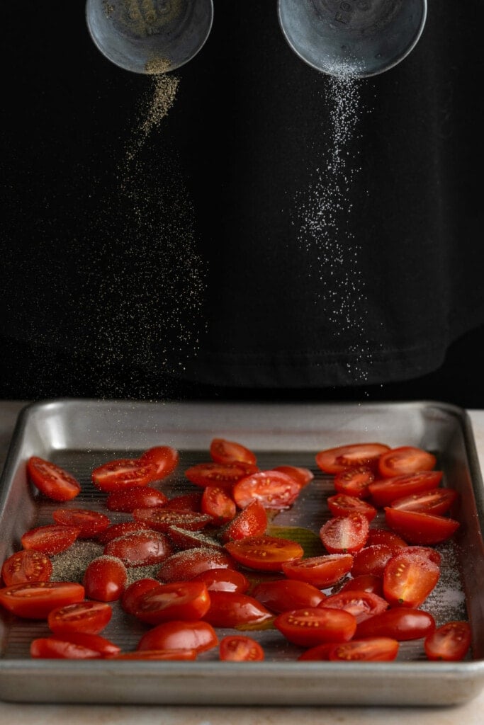 Adding salt and pepper to grape tomatoes to roast.