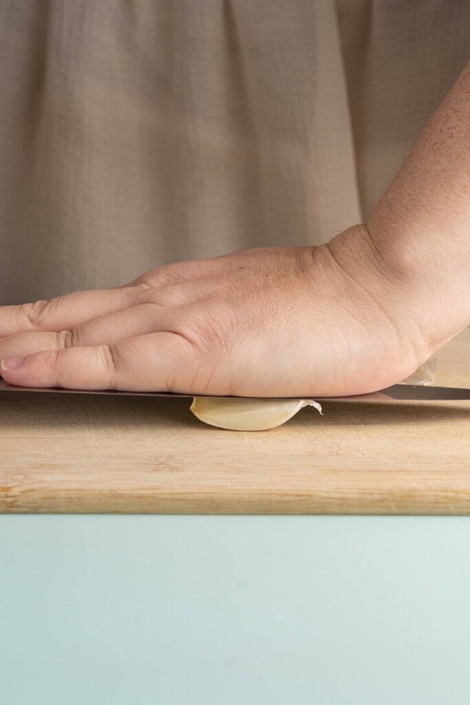 Using knife to crush garlic to peel and prep for roasting