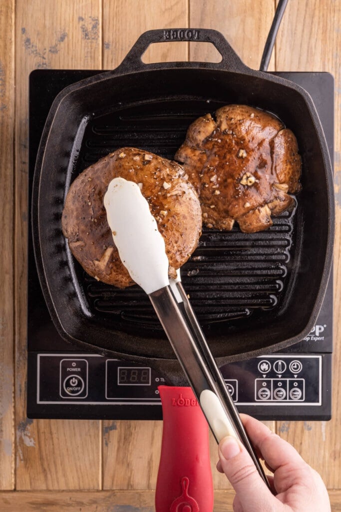 Using tongs to flip portobello mushrooms in grill pan