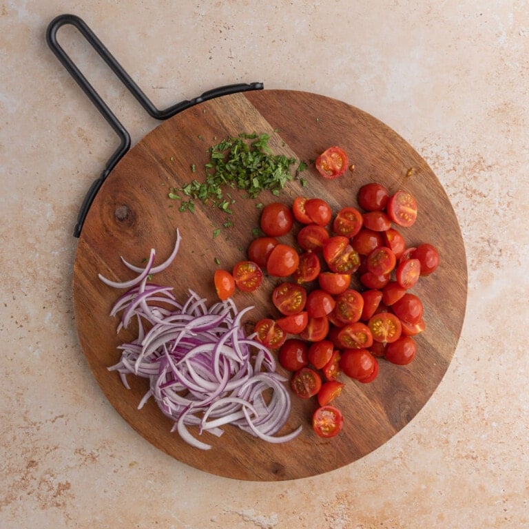 Chopped onions, tomatoes and herbs on a circular wooden chopping board
