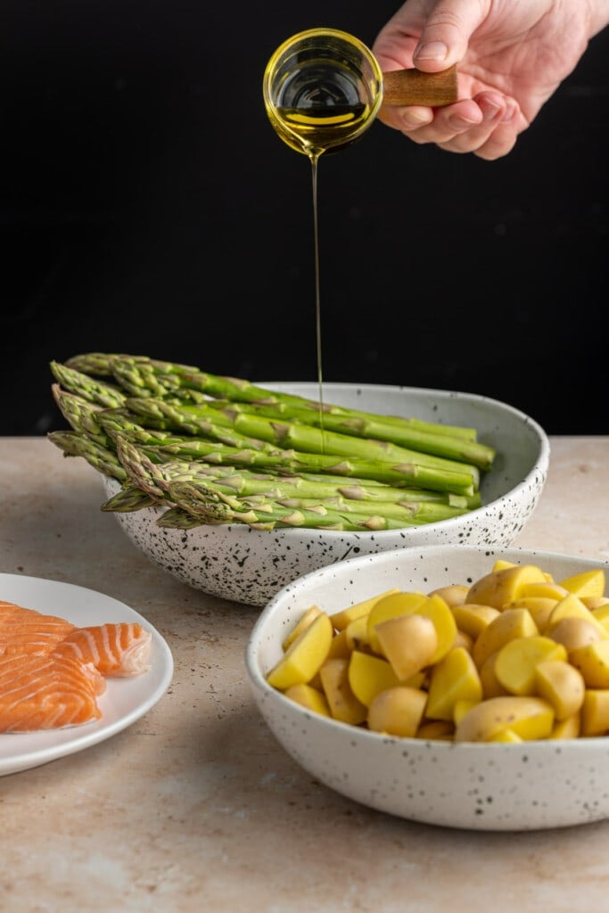 Adding olive oil to asparagus, potatoes, and salmon.
