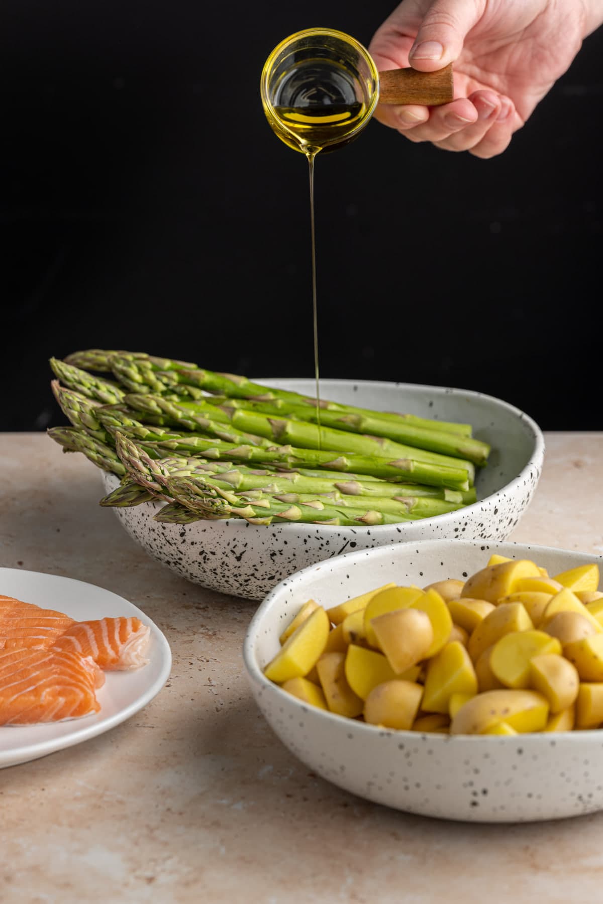 Adding olive oil to asparagus, potatoes, and salmon