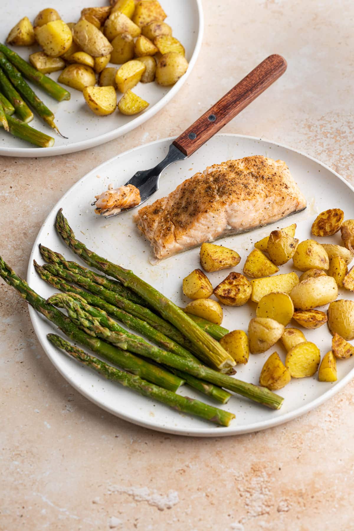 Salmon with forkful cut out on plate with asparagus and potatoes