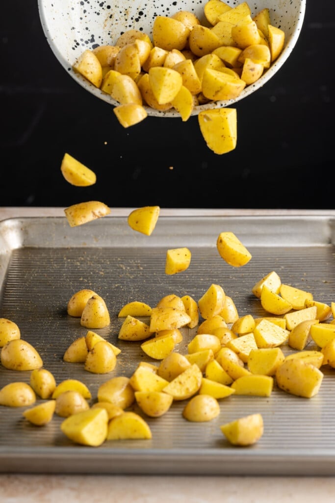 Adding chopped potatoes to a baking sheet.