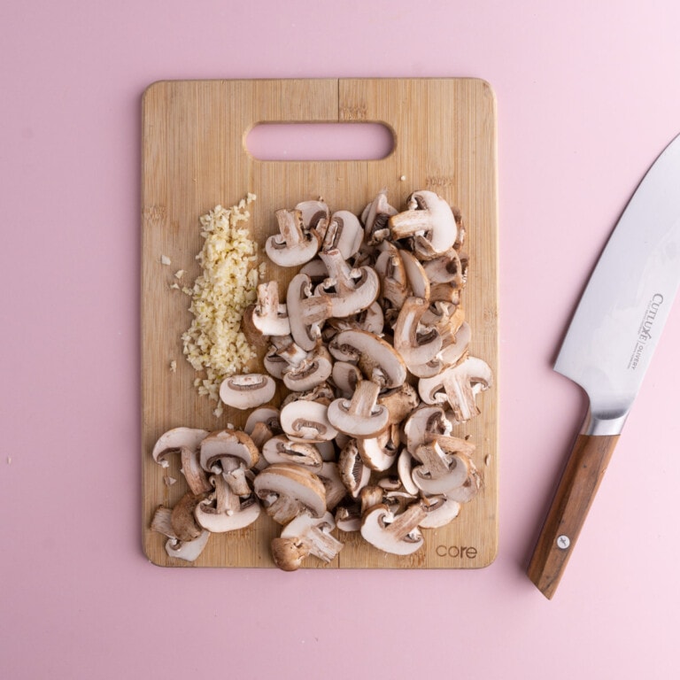 Sliced mushrooms and minced garlic on a cutting board