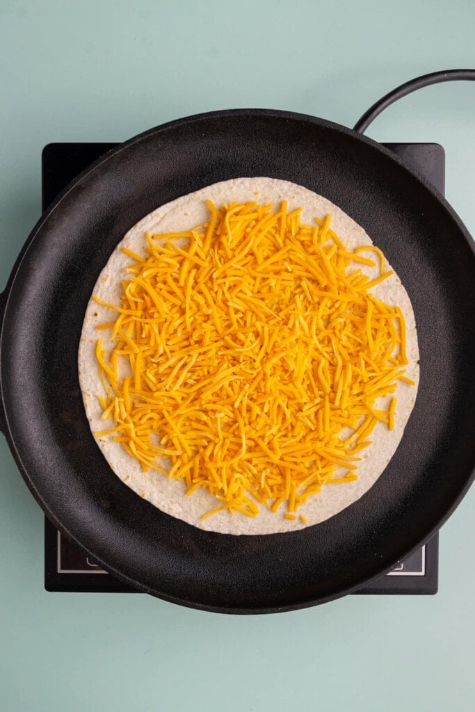 Large tortilla on a cast iron skillet with a layer of cheddar cheese
