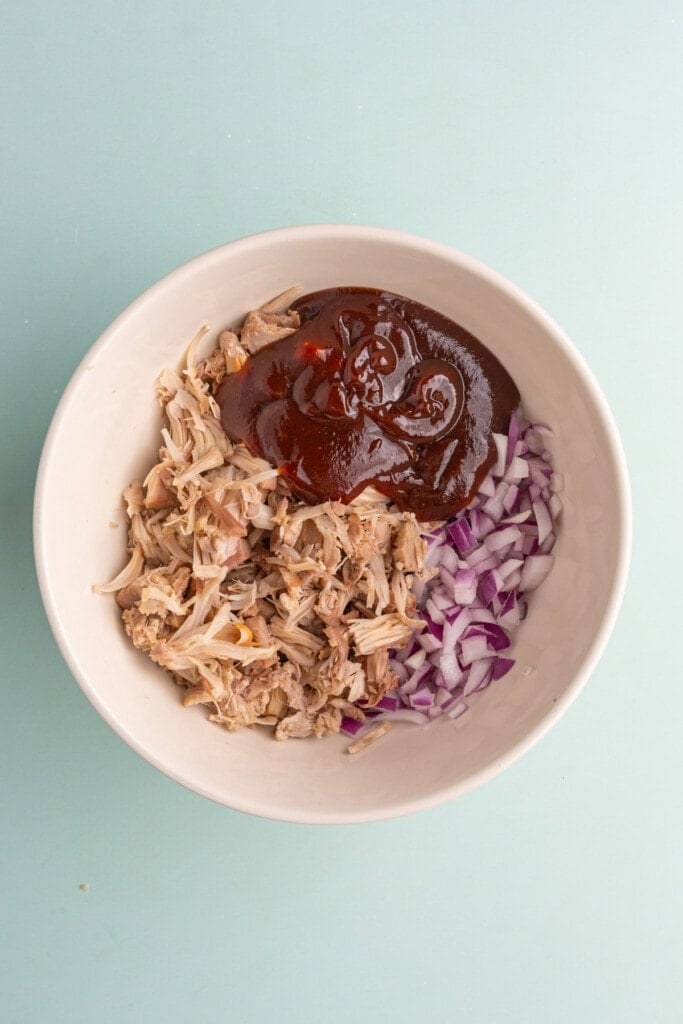 Adding shredded jackfruit to a large bowl with BBQ sauce and diced red onion