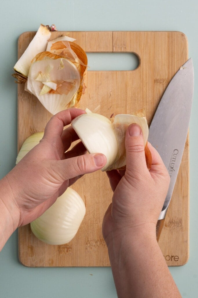 Peeling the outer layer of a yellow onion off to discard