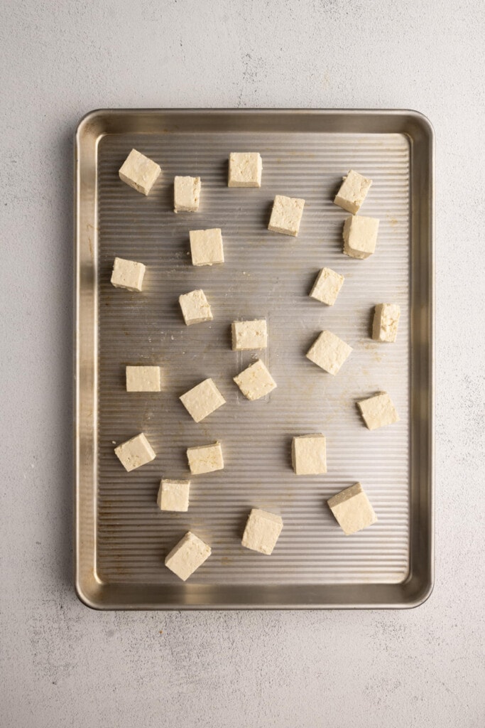 Adding cubed tofu coated with olive oil and cornstarch to a baking sheet