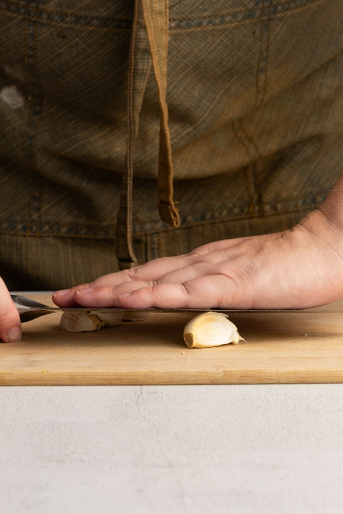 Crushing garlic with smooth side of the knife to make it easier to peel