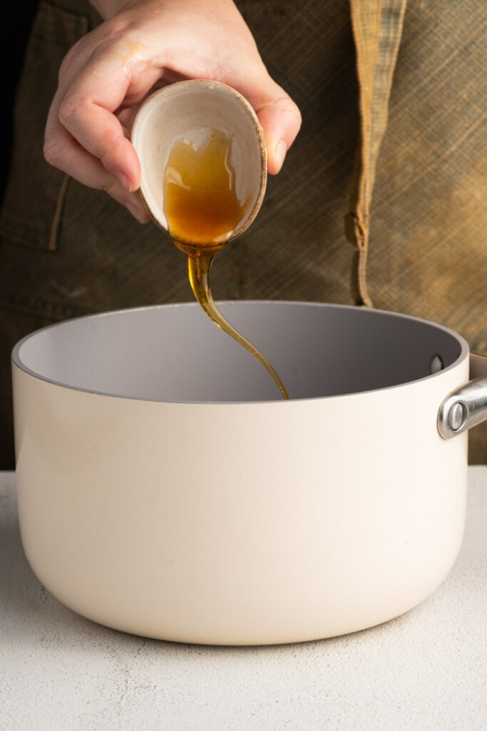Adding honey to a pot to make a sticky honey garlic sauce