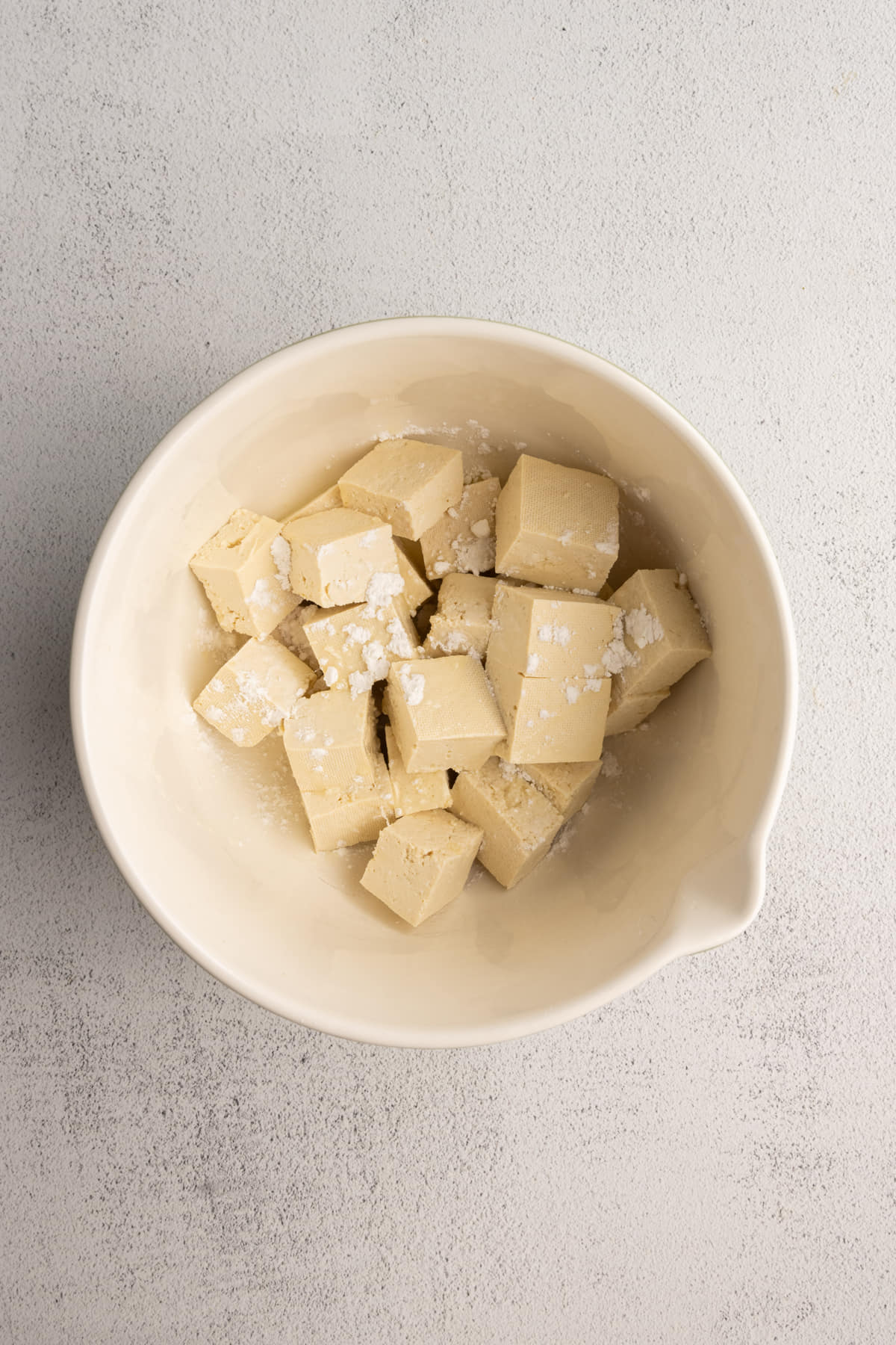 Adding cubed tofu to a mixing bowl to toss it with cornstarch and olive oil