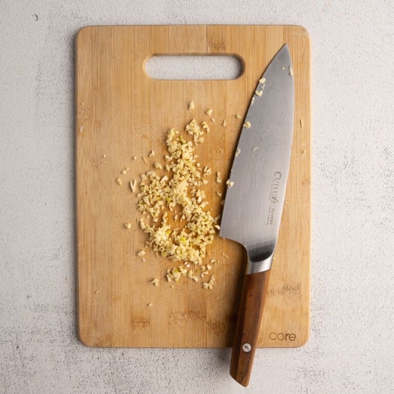 Mincing garlic on a cutting board with a sharp knife