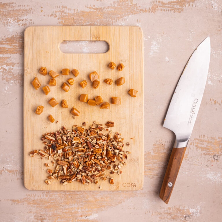 Chopped pecans and sliced chewy caramels on a cutting board