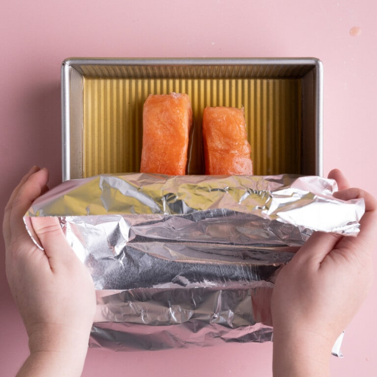 Covering frozen salmon in vegetable broth with aluminum foil