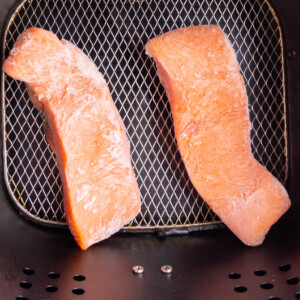 Two portions of frozen salmon in air fryer basket