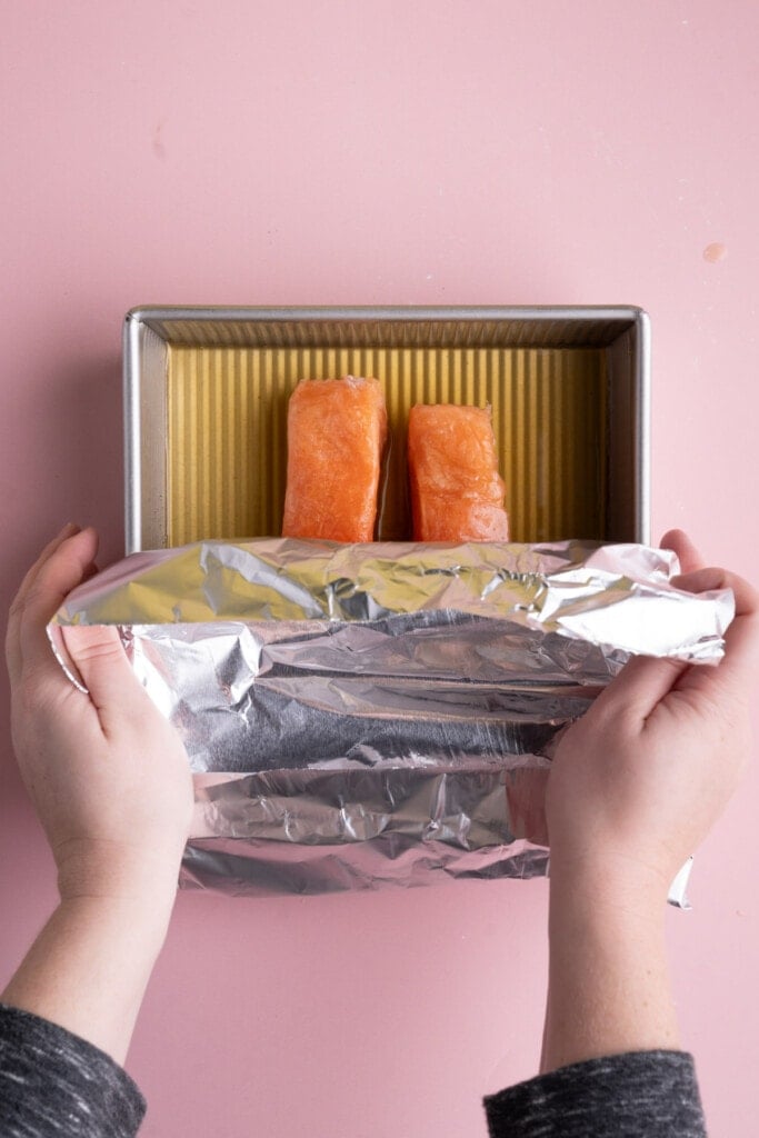 Covering dish with frozen salmon and vegetable broth with aluminum foil
