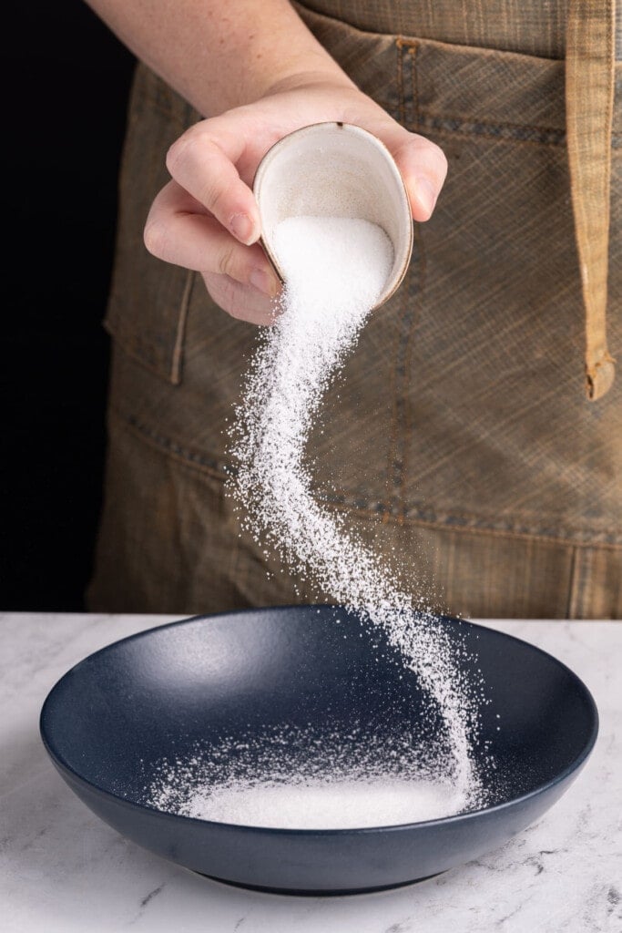 Adding granulated sugar to a shallow bowl to make lemon sugar