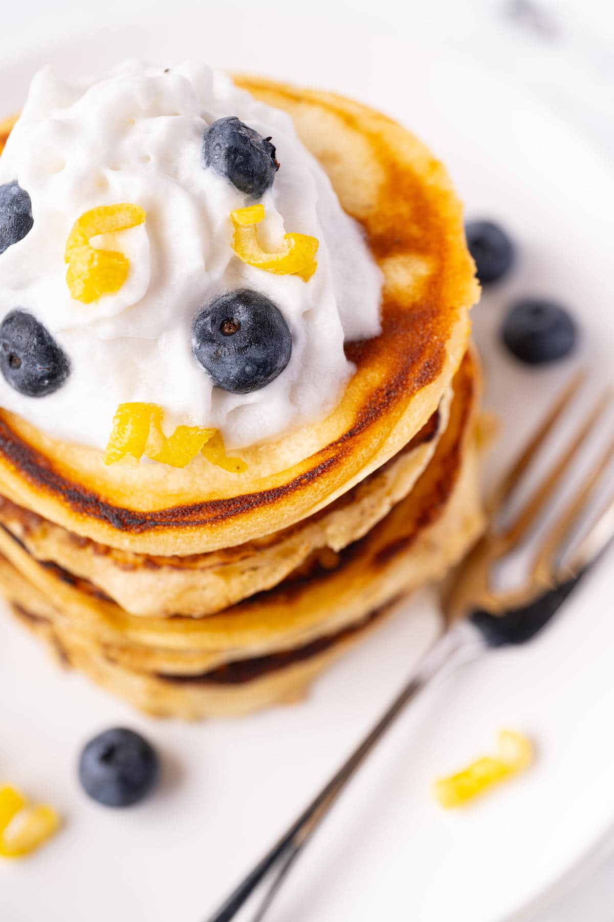 Close up shot of pancakes with whipped cream, lemon zest, and fresh blueberries