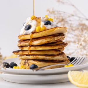 Stack of lemon pancakes with maple syrup being poured over it