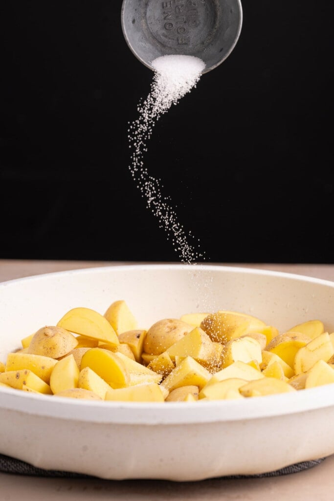 Adding salt to potatoes in a frying pan.