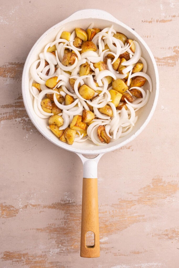 Adding sliced onions to pan with pan-fried potatoes