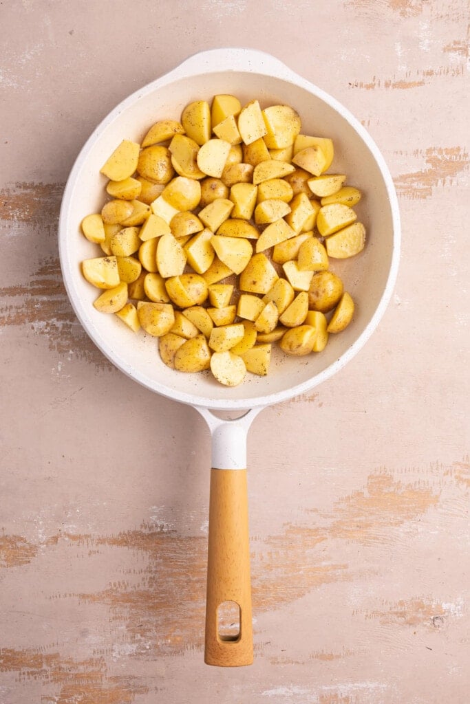 Potatoe wedges in a frying pan with olive oil, salt, and pepper