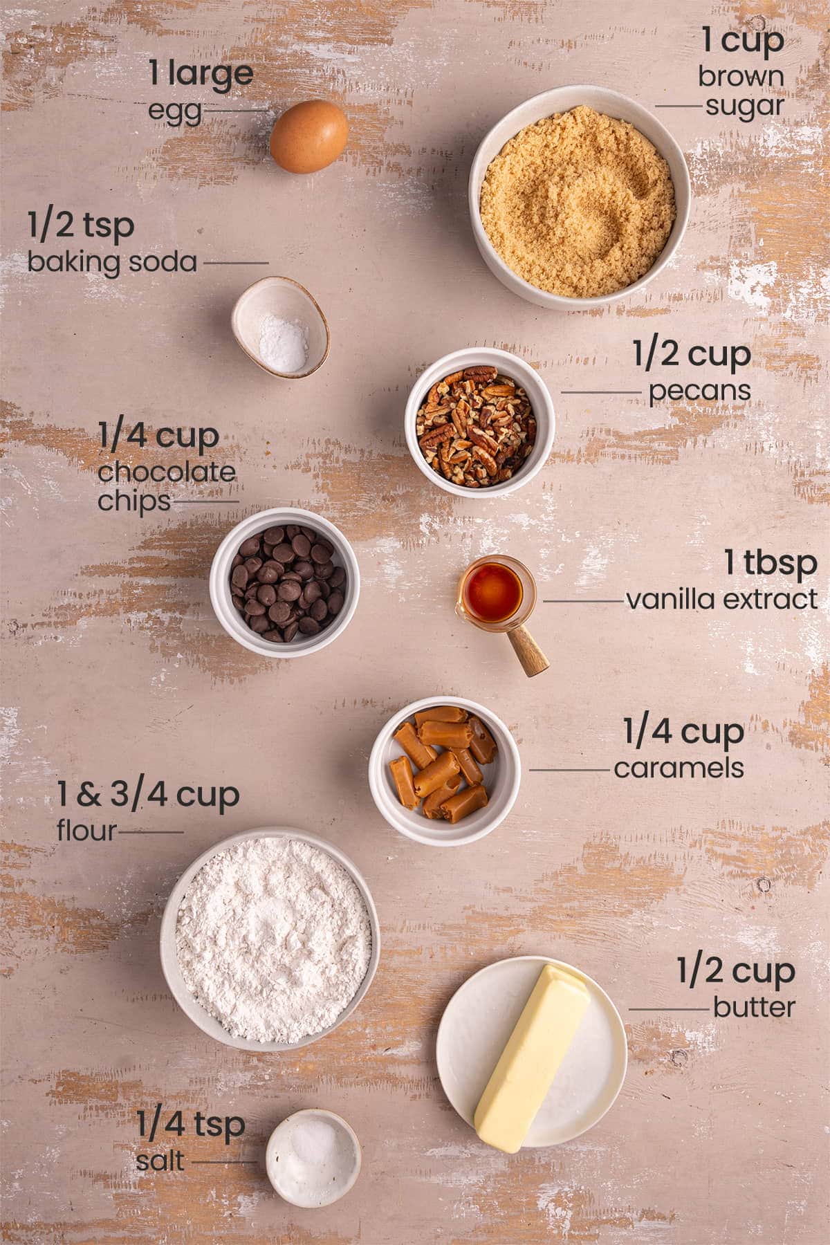ingredients for pecan caramel chocolate chip cookies - egg, brown sugar, baking soda, pecans, chocolate chips, vanilla extract, caramels, flour, butter, salt