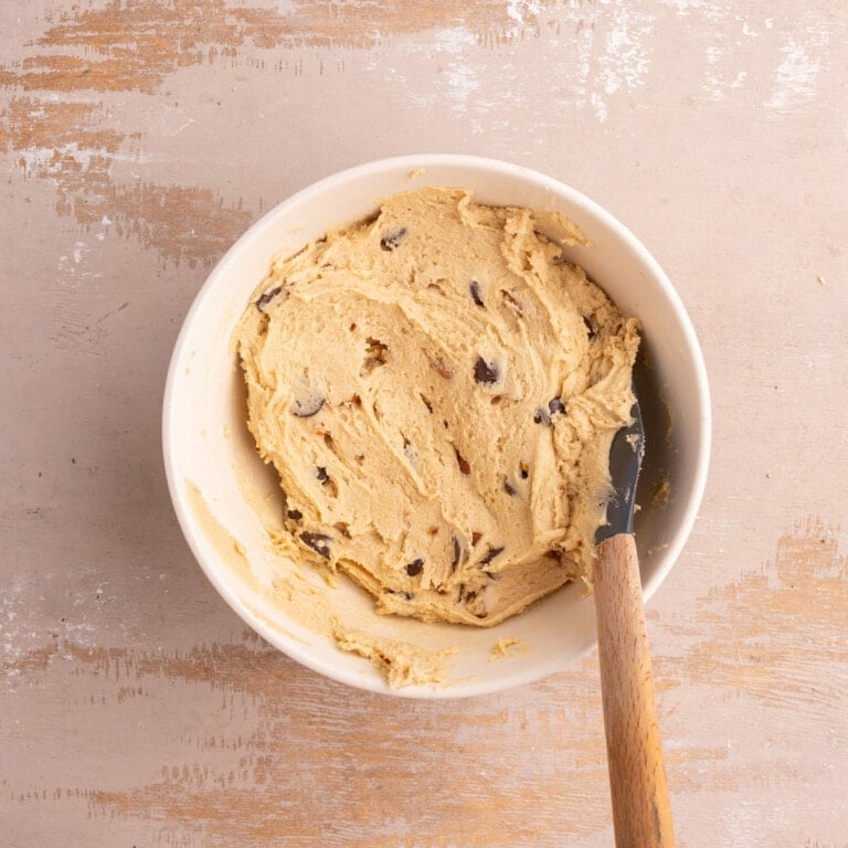 Using a rubber spatula to fold in pecans, caramel, and chocolate chips into cookie dough